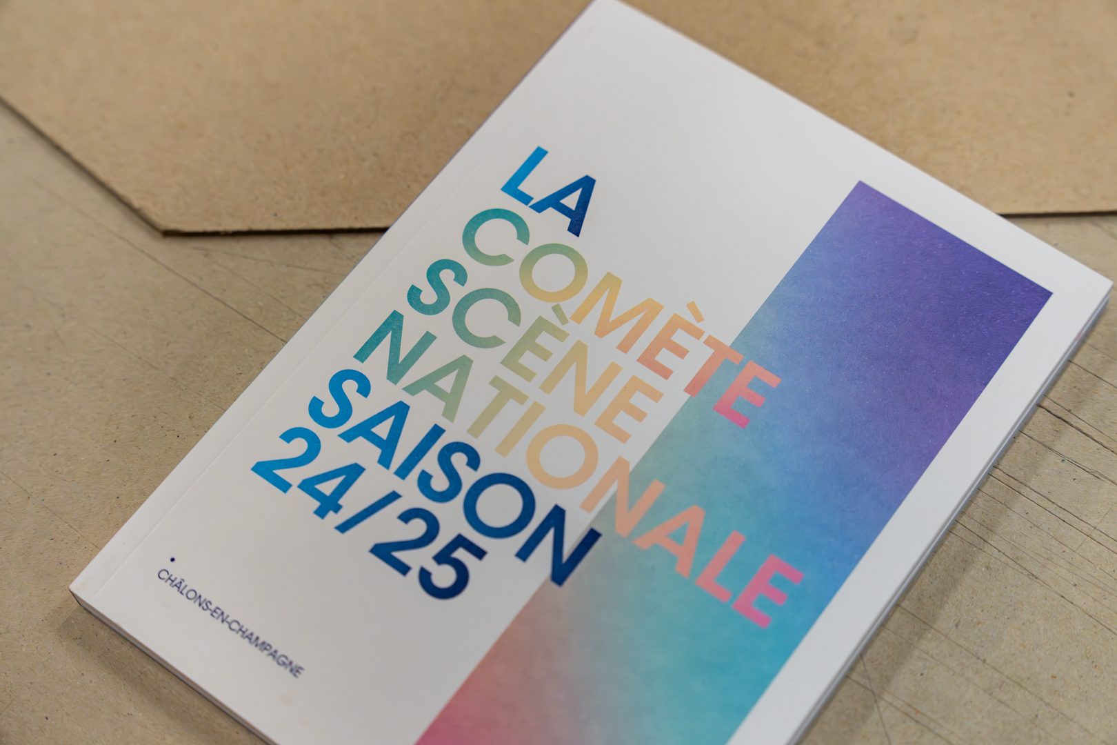 Brochure La Comète scène nationale saison 24-25 dans son enveloppe kraft